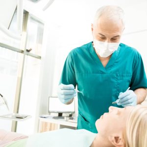 Professional dentist in uniform leaning over his patient before check-up with instruments